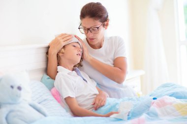 Hasta çocuk yatakta. Anne hasta çocuğu kontrol ediyor. Küçük çocuk kendini hasta hissediyor. Annem termometre ve öksürük şurubuyla. Genç hasta öksürüyor ve hapşırıyor. Grip önleme ve tedavi.