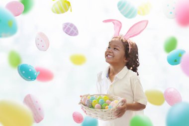 Çocuklar paskalya yumurtalarını boyuyor. Tavşan kulaklı çocuklar Paskalya avı için renkli yumurta boyuyorlar. Bahar tatili kutlaması için çiçek, sepet ve tavşanlı ev dekorasyonu. Küçük kıvırcık çocuk evi dekore ediyor..