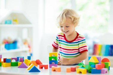 Çocuk renkli oyuncak bloklarıyla oynuyor. Küçük çocuk oyuncaklardan kule inşa ediyor. Küçük çocuklar için eğitici ve yaratıcı oyuncaklar ve oyunlar. Gökkuşağı tuğlalı beyaz yatak odasındaki bebek. Evdeki çocuk.