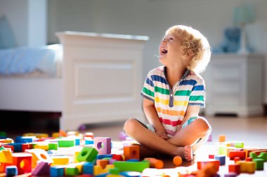 Çocuk renkli oyuncak bloklarıyla oynuyor. Çocuklar oynar. Küçük çocuk güneşli beyaz yatak odasındaki karanlık zeminde oyuncaklardan kule inşa ediyor. Bebek ve bebek için eğitici bir oyun. Çocuklar oyuncak ev yapar.