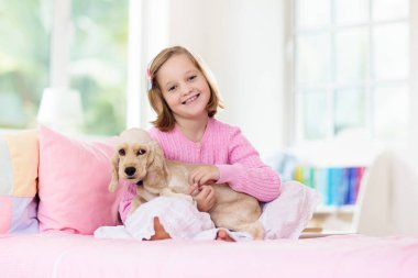 Bebek köpekle oynayan çocuk. Çocuklar köpek yavrusuyla oynar. Küçük kız ve Amerikan cocker spaniel evde yatakta. Çocuklar ve evcil hayvanlar evde. Çocuk evcil hayvanla şekerleme yapıyor. Hayvan bakımı.