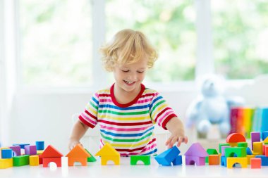 Çocuk renkli oyuncak bloklarıyla oynuyor. Küçük çocuk oyuncaklardan kule inşa ediyor. Küçük çocuklar için eğitici ve yaratıcı oyuncaklar ve oyunlar. Gökkuşağı tuğlalı beyaz yatak odasındaki bebek. Evdeki çocuk.