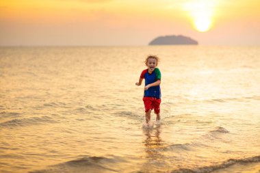 Okyanus sahilinde oynayan bir çocuk. Gün batımında dalgalara atlayan bir çocuk. Aile için deniz tatili. Yaz tatili boyunca egzotik adada koşan küçük çocuk.. 