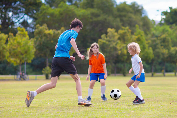 Дети играют в футбол на открытом поле. Дети забивают гол на футбольном матче. Девочка и мальчик пинают мяч. Бег ребенка в командной майке и бутсах. Школьный футбольный клуб. Спортивная подготовка для молодого игрока.