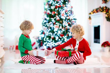 Noel arifesinde Noel ağacı ve şömine başında çocuklar. Noel 'i evde kutlayan çocuklu bir aile. Erkek ve kız aynı pijamaları giyip Noel ağacını süslüyor ve hediyeleri açıyor. Çocuklar için tatil hediyeleri.