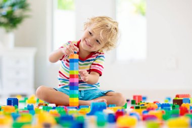 Çocuk renkli oyuncak bloklarıyla oynuyor. Küçük çocuk evde ya da kreşte kule inşa ediyor. Küçük çocuklar için eğitici oyuncaklar. Bebek ya da bebek için inşaat bloğu. Anaokulundaki oyun odasında karışıklık..