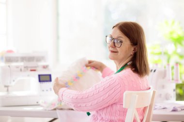 Beyaz masada dikiş diken bir kadın. Moda tasarım atölyesi. Yaratıcı hobi ve el sanatları. El yapımı giysiler. Kilitli makineli terzi ya da terzi. Kadın elbise yapıyor. Ekipman ve araçları dik