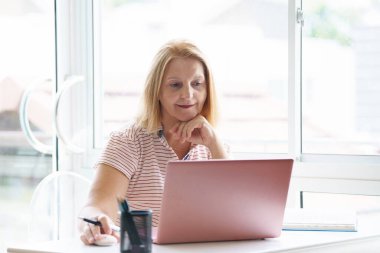 Dizüstü bilgisayarı ve cep telefonu olan bir kadın. Güneşli modern ofiste çalışan güzel, mutlu bir kadın. İşyerinde serbest çalışan biri. Emeklilik yaşı eğitimi. Online alışveriş ve bankacılık.