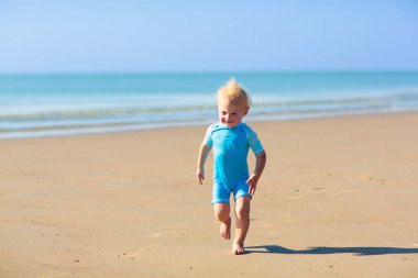 Tropik plajda oynayan çocuklar. Su sıçratma eğlencesi. Deniz dalgalarında süzülen küçük çocuk. Çocuklar yaz tatilinde yüzer ve oynarlar. Kum ve su oyuncağı, küçük çocuklar için güneş koruması.. 