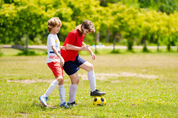 Ребенок играет в футбол. Дети играют в футбол на открытом поле. Мальчик пинает мяч в летнем парке. Здоровый образ жизни для маленьких детей. Школьный спортивный клуб. Юниорская лига.