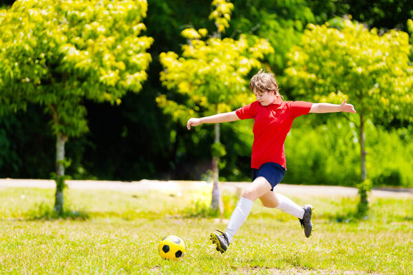 Ребенок играет в футбол. Дети играют в футбол на открытом поле. Девочка-подросток пинает мяч в летнем парке. Здоровый образ жизни для маленьких детей. Школьный спортивный клуб. Юниорская лига.