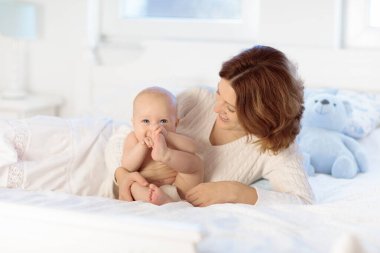 Anne ve çocuk beyaz bir yatakta. Anne ve bebek çocuk bezi güneşli yatak odasında oynarken. Ebeveyn ve çocuk evde rahatlatıcı. Aile birlikte eğleniyor. Yatak ve bebek kreş Tekstil.