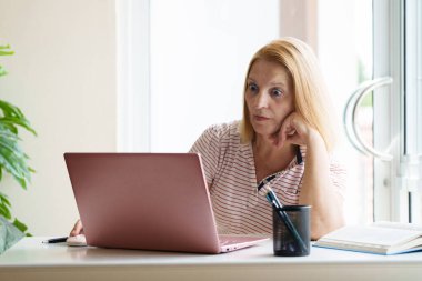 Dizüstü bilgisayarı ve cep telefonu olan bir kadın. Güneşli modern ofiste çalışan güzel, mutlu bir kadın. İşyerinde serbest çalışan biri. Emeklilik yaşı eğitimi. Online alışveriş ve bankacılık.