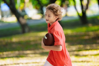 Amerikan futbolu oynayan bir aile. Çocuklar güneşli yaz parkında rugby oynuyorlar. Baba ve çocuklar top oynar, koşar ve güler. Sağlıklı açık hava sporları aktivitesi.