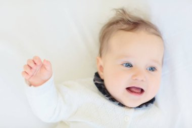 Beyaz güneşli yatak odasında sevimli bir bebek. Yeni doğmuş çocuk yatakta dinleniyor. Küçük çocuklar için çocuk odası. Çocuklar için tekstil ve yatak. Aile sabahı evde. Oyuncak ayıyla karnını doyururken doğan yeni çocuk..