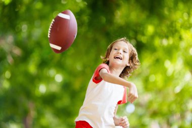 Amerikan futbolu oynayan bir aile. Çocuklar güneşli yaz parkında rugby oynuyorlar. Baba ve çocuklar top oynar, koşar ve güler. Sağlıklı açık hava sporları aktivitesi.