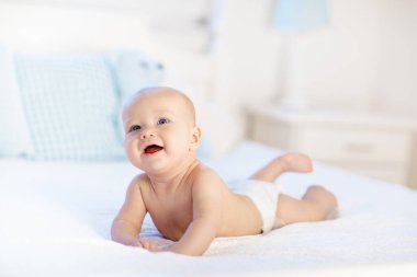 Beyaz güneşli yatak odasında sevimli bir bebek. Yeni doğmuş çocuk yatakta dinleniyor. Küçük çocuklar için çocuk odası. Çocuklar için tekstil ve yatak. Aile sabahı evde. Oyuncak ayıyla karnını doyururken doğan yeni çocuk..