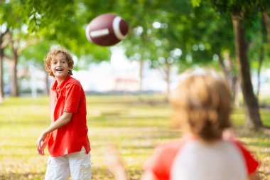 Amerikan futbolu oynayan bir aile. Çocuklar güneşli yaz parkında rugby oynuyorlar. Baba ve çocuklar top oynar, koşar ve güler. Sağlıklı açık hava sporları aktivitesi.