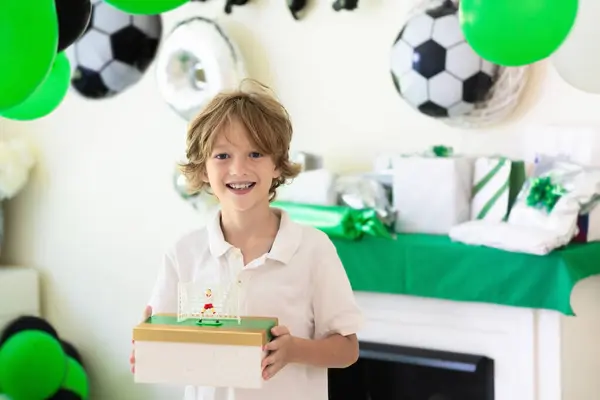 stock image Kids birthday. Football theme child party. Little boy holding gift box and balloon on his birthday morning. Soccer and sports decoration. Children open present.