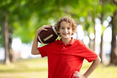 Amerikan futbolu oynayan bir aile. Çocuklar güneşli yaz parkında rugby oynuyorlar. Baba ve çocuklar top oynar, koşar ve güler. Sağlıklı açık hava sporları aktivitesi.
