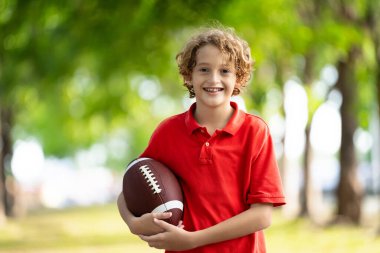 Amerikan futbolu oynayan bir aile. Çocuklar güneşli yaz parkında rugby oynuyorlar. Baba ve çocuklar top oynar, koşar ve güler. Sağlıklı açık hava sporları aktivitesi.