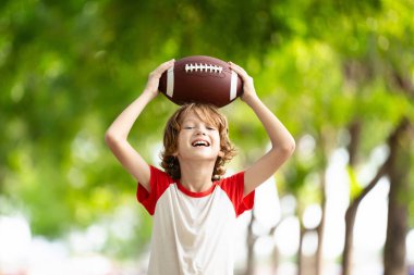 Amerikan futbolu oynayan bir aile. Çocuklar güneşli yaz parkında rugby oynuyorlar. Baba ve çocuklar top oynar, koşar ve güler. Sağlıklı açık hava sporları aktivitesi.