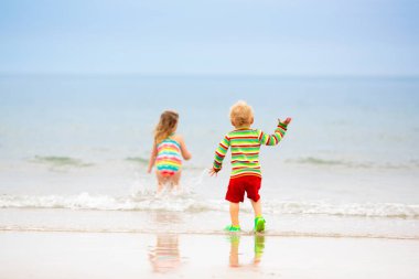 Tropik plajda oynayan çocuklar. Çocuklar yaz tatilinde yüzer ve denizde oynarlar. Kum ve su eğlencesi, küçük çocuklar için güneş koruması. Küçük bebek okyanus kıyısında koşuyor ve zıplıyor.
