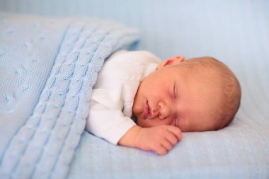 Yeni doğan bebek yatakta. Yeni doğan çocuk mavi örgü battaniye altında uyuyor. Çocuk uyku. Çocuklar için yatak takımları. Bebek yatakta uyuyor. Sağlıklı çocuk doğumdan kısa bir süre sonra. Kablo Tekstil Örme.