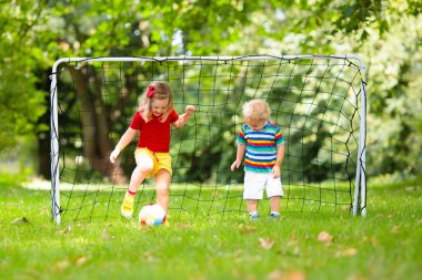 Çocuk futbol oynuyor. Çocuklar dışarıda futbol oynarlar. Küçük kız ve oğlan yaz parkında top oynuyorlar. Küçük çocuklar için sağlıklı bir aktivite. Okul spor kulübü takımı. Futbol Küçükler Ligi.