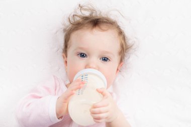 Beyaz güneşli yatak odasında sevimli bir bebek. Yeni doğmuş çocuk yatakta dinleniyor. Küçük çocuklar için çocuk odası. Çocuklar için tekstil ve yatak. Aile sabahı evde. Oyuncak ayıyla karnını doyururken doğan yeni çocuk..