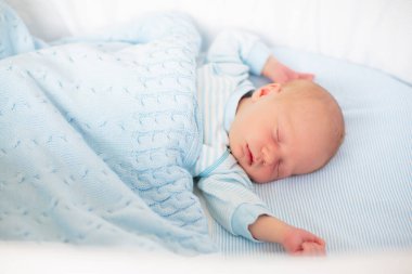 Yeni doğan bebek yatakta. Yeni doğan çocuk mavi örgü battaniye altında uyuyor. Çocuk uyku. Çocuklar için yatak takımları. Bebek yatakta uyuyor. Sağlıklı çocuk doğumdan kısa bir süre sonra. Kablo Tekstil Örme.