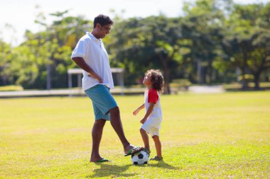 Baba ve oğlu futbol oynuyor. Baba ve küçük çocuk futbol oynuyorlar. Genç aktif aile açık havada güneşli bir yaz gününün tadını çıkarıyor. Çocuklar için sağlıklı bir spor. Futbol kulübü..