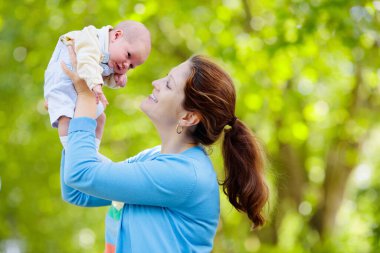 Bir park Holding yeni doğan bebek anne. Yeni doğan oğluyla bahçede oynayan anne. Aile çocuklarla oynamak açık havada. Genç kadın küçük çocuk sarılma. Ebeveynler ve çocuklar yaz aylarında eğleniyor.