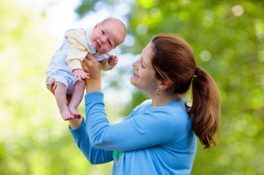 Bir park Holding yeni doğan bebek anne. Yeni doğan oğluyla bahçede oynayan anne. Aile çocuklarla oynamak açık havada. Genç kadın küçük çocuk sarılma. Ebeveynler ve çocuklar yaz aylarında eğleniyor.