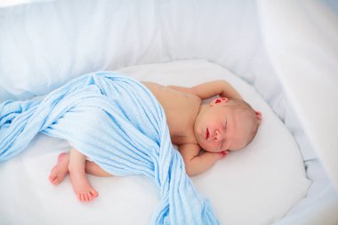 Beyaz güneşli yatak odasında sevimli bir bebek. Yeni doğmuş çocuk yatakta dinleniyor. Küçük çocuklar için çocuk odası. Çocuklar için tekstil ve yatak. Aile sabahı evde. Oyuncak ayıyla karnını doyururken doğan yeni çocuk..