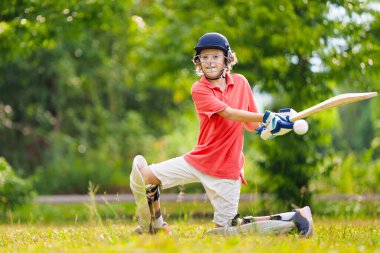 Yaz parkında kriket oynayan çocuklar. Kriket sahasında beyzbol sopası ve topu olan çocuk. Güvenli oyun için kask ve koruma. Aktif çocuklar için spor. Okul çocukları için kriket kulübü. Spor aktivitesi ve egzersiz.