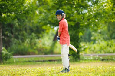 Yaz parkında kriket oynayan çocuklar. Kriket sahasında beyzbol sopası ve topu olan çocuk. Güvenli oyun için kask ve koruma. Aktif çocuklar için spor. Okul çocukları için kriket kulübü. Spor aktivitesi ve egzersiz.