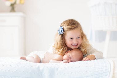 Küçük kız kardeşim yeni doğan kardeşi sarılma. Yürümeye başlayan çocuk toplantı yeni kardeş. Sevimli kız ve erkek yeni doğan bebek beyaz bir yatak odasında rahatlayın. Çocuklu evde aile. Aşk, güven ve hassasiyet kavramı. 