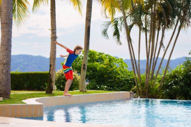 Bir grup çocuk havuza atlıyor. Yaz suyu eğlencesi. Çocuklar açık havuzda oynarlar. Genç bir çocukla yaz tatili. Tropik tatil beldesinde tatil. Çocukla seyahat et..