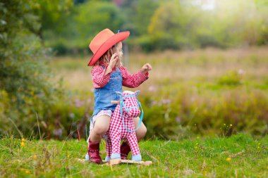 Küçük erkek ve kız kovboy ve oyuncak sallanan at Park ile oynarken cowgirl gibi giyinmiş. Çocuklar açık havada oynar. Çocuklarda Cadılar Bayramı kostümleri oyun ya da şeker. Okul öncesi veya yürümeye başlayan çocuk için oyuncaklar