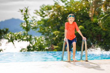 Bir grup çocuk havuza atlıyor. Yaz suyu eğlencesi. Çocuklar açık havuzda oynarlar. Genç bir çocukla yaz tatili. Tropik tatil beldesinde tatil. Çocukla seyahat et..