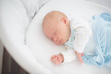 Beyaz güneşli yatak odasında sevimli bir bebek. Yeni doğmuş çocuk yatakta dinleniyor. Küçük çocuklar için çocuk odası. Çocuklar için tekstil ve yatak. Aile sabahı evde. Oyuncak ayıyla karnını doyururken doğan yeni çocuk..