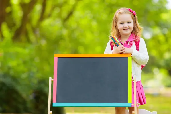 stock image Children happy to be back to school. Preschooler girl and boy with backpack and books at black chalk board learning to write letters and read. Kids at preschool or kindergarten learn the alphabet.