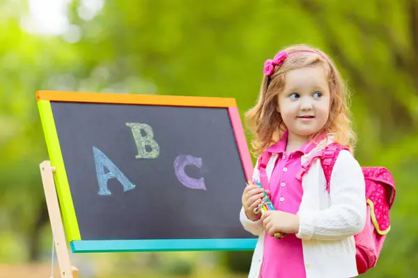 stock image Children happy to be back to school. Preschooler girl and boy with backpack and books at black chalk board learning to write letters and read. Kids at preschool or kindergarten learn the alphabet.