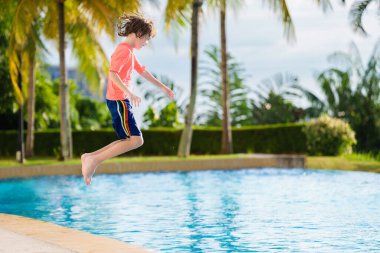 Bir grup çocuk havuza atlıyor. Yaz suyu eğlencesi. Çocuklar açık havuzda oynarlar. Genç bir çocukla yaz tatili. Tropik tatil beldesinde tatil. Çocukla seyahat et..