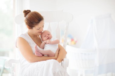 Yeni doğmuş bebeği olan genç bir anne. Annesi küçük bebeğini emziriyor. Aile evde. Çocuk bakımı. Çocukların sağlığı için emziriyorum. Küçük çocuk için beyaz yatak odası.