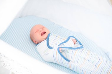 Yeni doğmuş bir çocuğu sarıp sarmalamak. Kundak battaniyeli bebek. Uyumak için sarılı ağlayan bir bebek. Yatakta aç bir bebek.