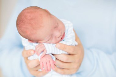 Baba kucağında yeni doğmuş bir çocuk. Mavi örgü battaniyenin altında uyuyan yeni doğmuş bir çocuk. Çocuklar uyur. Baba kucağında bebek var. Doğumdan kısa bir süre sonra sağlıklı küçük bir çocuk. 