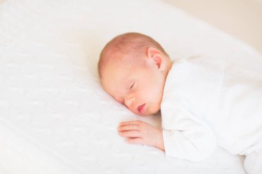 Beyaz güneşli yatak odasında sevimli bir bebek. Yeni doğmuş çocuk yatakta dinleniyor. Küçük çocuklar için çocuk odası. Çocuklar için tekstil ve yatak. Aile sabahı evde. Oyuncak ayıyla karnını doyururken doğan yeni çocuk..