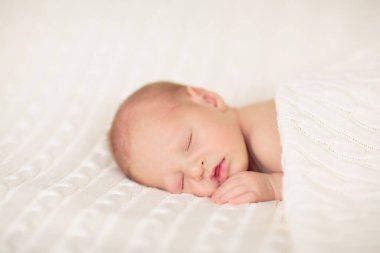 Beyaz güneşli yatak odasında sevimli bir bebek. Yeni doğmuş çocuk yatakta dinleniyor. Küçük çocuklar için çocuk odası. Çocuklar için tekstil ve yatak. Aile sabahı evde. Oyuncak ayıyla karnını doyururken doğan yeni çocuk..